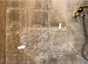 Sample refinishing test area on an etched marble shower wall showing marble honing and restoration in progress.