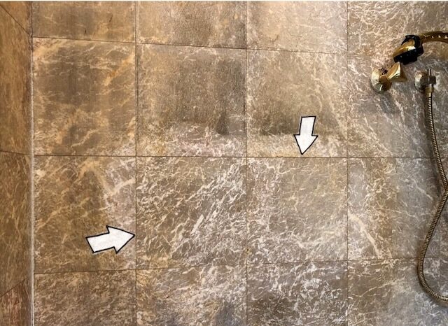 Sample refinishing test area on an etched marble shower wall showing marble honing and restoration in progress.
